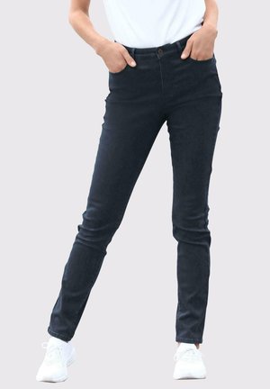 Donkerblauwe skinny jeans met een middelhoge tailleband, zakken aan de voorkant en een knoopsluiting, gecombineerd met witte sportschoenen.