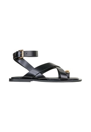 Sandalo piatto in pelle nera con cinturino alla caviglia e fibbia dorata, con cinturini incrociati sulle dita e dettaglio borchiato dorato sull'anello dell'alluce.