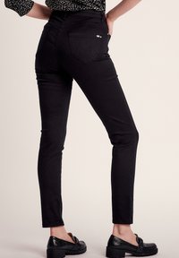 Zwarte slim-fit jeans met een hoge taille, met een gladde textuur, twee achterzakken en gestikte details aan de zijkanten.