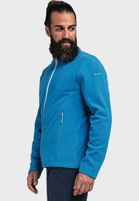 Niebieska polarowa kurtka z pełnym zamkiem błyskawicznym, wysokim kołnierzem i dwoma kieszeniami na zamek. Posiada subtelne logo na prawym rękawie. Miękka tekstura.