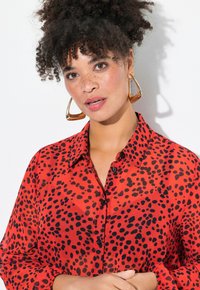 Blusa roja de manga larga con patrón de manchas negras. Cuenta con una parte delantera abotonada y cuello, hecha de un tejido ligero con una textura suave.