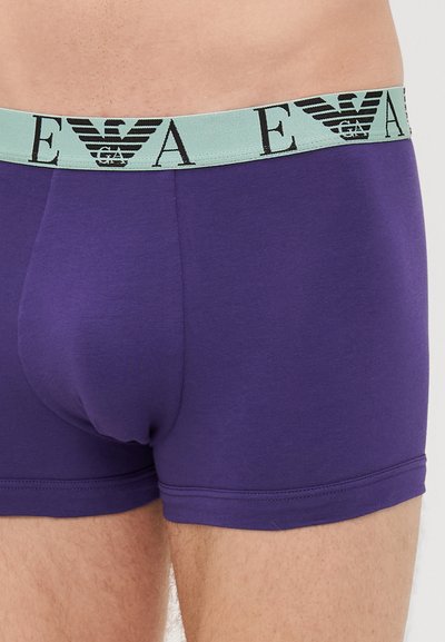 Lila boxer alsónadrág széles világoskék derékpánttal, fekete logóbetűzéssel. Simább anyag, testhezálló kivitel.