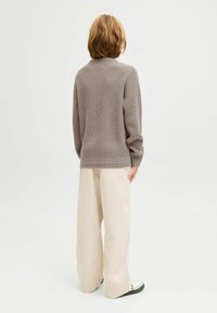 Hellgrauer Strickpullover mit einem strukturierten Muster, kombiniert mit weiten beigen Hosen und Schwarz-Weiß-Sneakers, von hinten betrachtet.
