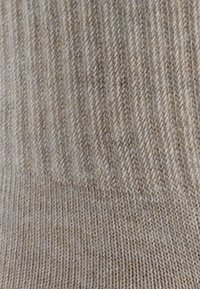 Beżowa dzianina w prążki z delikatną teksturą; posiada pionowe paski i miękki, elastyczny materiał, odpowiedni do skarpet lub codziennych ubrań.