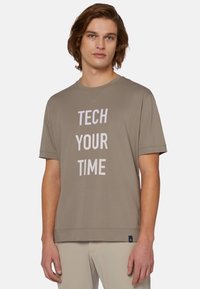 Krátký rukáv, béžové bavlněné tričko s velkým bílým nápisem "TECH YOUR TIME." Má kulatý výstřih a uvolněný střih. Bez viditelných vzorů.