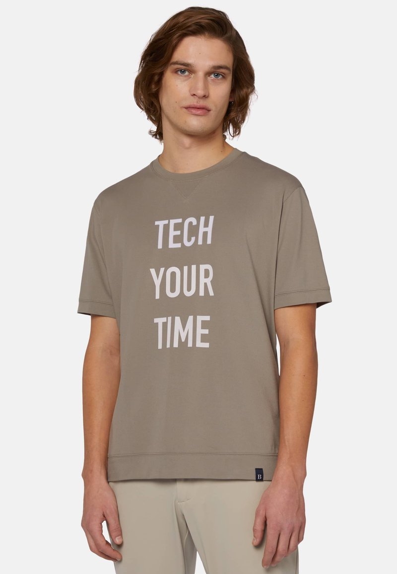 Krátký rukáv, béžové bavlněné tričko s velkým bílým nápisem "TECH YOUR TIME." Má kulatý výstřih a uvolněný střih. Bez viditelných vzorů.