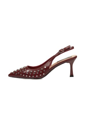Tacón slingback de cuero rojo con punta afilada, adornado con tachuelas plateadas. Cuenta con un tacón esbelto y una correa ajustable en el tobillo.