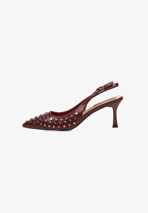 Tacón slingback de cuero rojo con punta afilada, adornado con tachuelas plateadas. Cuenta con un tacón esbelto y una correa ajustable en el tobillo.