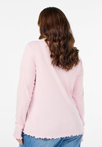 Švelnios rožinės spalvos ilgomis rankovėmis marškiniai su banguotu kraštu ir rankogaliais, pagaminti iš lengvo audinio. Atrodo atsipalaidavęs siluetas ir sklandus tekstūros vaizdas iš nugaros.