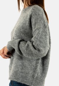 Suéter de punto gris con un escote de cuello redondo, dobladillo acanalado y tela texturizada. Corte holgado con hombros caídos y mangas largas, ligeramente enrolladas.