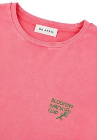 Roosa puuvillane T-särk ümarate kaelustega, millel on roheline broderi tekst "BLOOMING KARMA CLUB" ja lille graafika vasakul rinnaosal.
