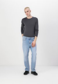 Gray long-sleeve t-shirt paired with light blue jeans and black sneakers. The outfit features a fitted design and simple stitching.