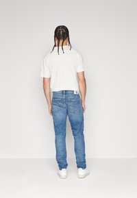 Vit t-shirt med kort ärm i kombination med ljusblå slim-fit jeans. Vita sneakers ger kontrast. Enkelt design med synliga sömnadsdetaljer.