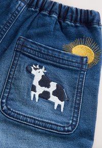 Denimshorts med elastisk talje, med en baglomme pyntet med marineblåt og hvidt kvægbroderi samt et gult solmotiv.