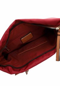 Red fabric bag interior with a smooth texture. Features a brown leather label, a zip pocket, and a slip pocket on one side.