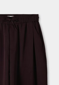 Pantalones negros plisados con cintura elástica y cierre de cordón; tela suave y ligera; cuenta con bolsillos laterales.