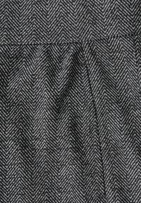 Harmaa ja musta kalanruotokuvioinen kangas, jossa on tekstuuri, ja joka sisältää laskoksia, jotka luovat pehmeitä taitteita ja liikettä.