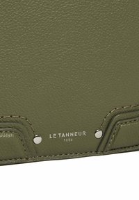 Prodotto in pelle verde oliva con superficie testurizzata, dettagli in hardware argentato e branding impressa "LE TANNEUR 1898" con cuciture a contrasto.