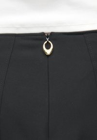 Pantaloni negri cu o textură netedă, fermoar frontal cu un inel de aur pentru tragere și linii curate, croite.