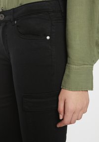 Mustad denim cargo püksid, millel on küljetasku ja hõbedane riistvara. Kombineeritud rohelise, pika varrukaga, nööbitud särgiga. Pehme tekstuur.
