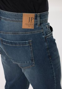 Vaqueros de mezclilla en azul oscuro con una etiqueta de cuero que dice "JP 1880". Presenta costuras en contraste y un diseño clásico de bolsillo.
