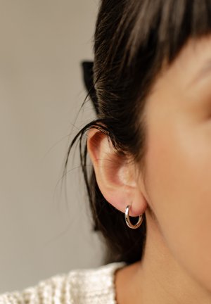 Boucle d'oreille en argent sur l'oreille d'un modèle, avec une finition lisse et brillante et un design circulaire ; les cheveux sont coiffés en arrière du visage.