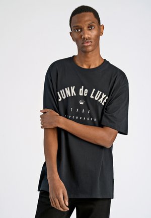 Camiseta de algodón negra con "JUNK de LUXE" impreso en blanco en el pecho, con cuello redondo y mangas cortas.