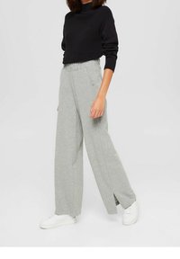 Pantaloni da jogging grigi a gamba larga con vita elastica, fessure laterali e maglione cropped nero a maglia testurizzata. Abbinati a sneaker bianche.