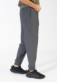 Graue Sporthosen mit elastischen Bündchen, Seitentaschen und einem glatten, leichten Stoff, kombiniert mit schwarzen Sneakers mit strukturiertem Design.