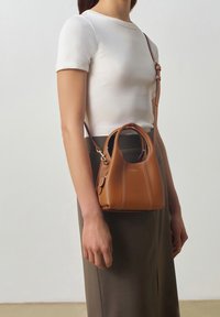 Brown leather handbag with a structured shape, featuring contrast stitching and a short handle, worn crossbody with an adjustable strap.
