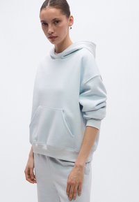 Sweatshirt azul-claro oversize feita de tecido macio, com bolso frontal, punhos canelados e corte descontraído. Textura suave, design minimalista.