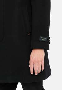 Cappotto nero in cashmere e lana con design monopetto, quattro bottoni sulla manica e tasca laterale. Etichetta visibile sulla manica.