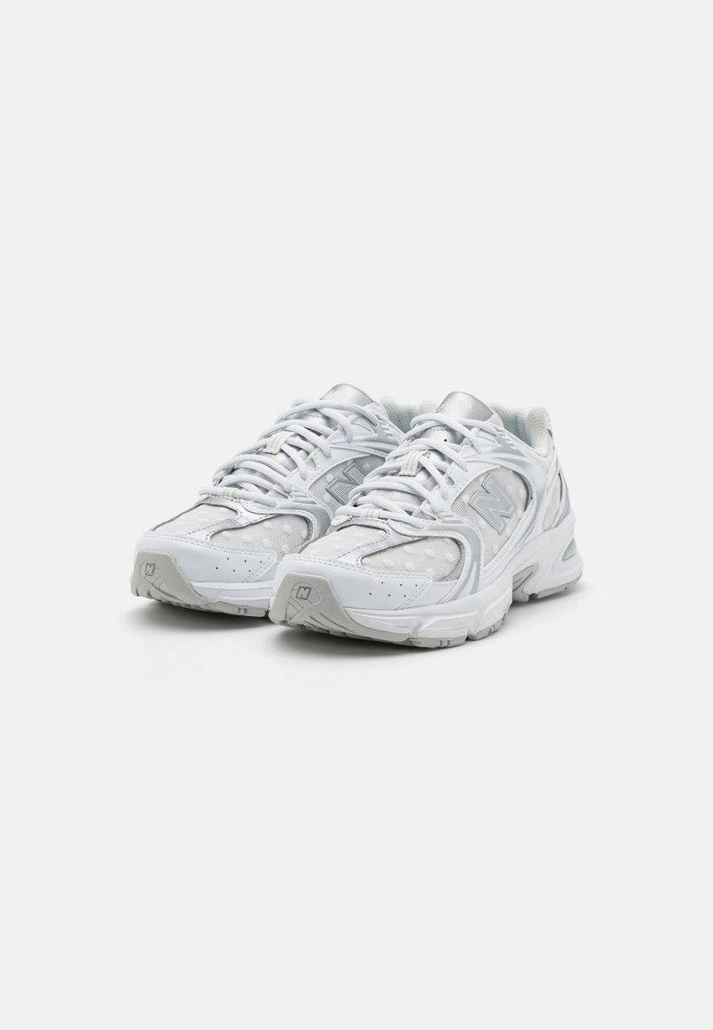 Chaussures de course blanches avec un dessus en maille texturée, des accents argentés, des coutures tonales et une semelle rembourrée. Présente un logo prominent sur le côté.
