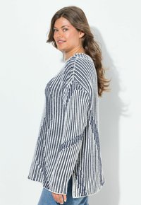 Maglione a righe in navy e bianco, caratterizzato da una vestibilità ampia, maniche larghe e un motivo a maglia strutturato. Abbinato a jeans in denim.