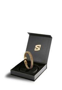 Goldener geflochtener Armband in einer schwarzen Box mit einem Samt-Inlay. Die Box zeichnet sich durch ein elegantes Design und ein goldenes Logo auf der Innenseite des Deckels aus.