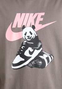 Grå T-skjorte med et tegneseriepanter på en svart-hvitt sneakers, med fet rosa "NIKE"-logo over. Enkel design med kontrasterende farger.