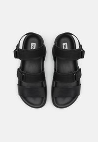 Sandales noires avec une semelle intérieure en cuir lisse, deux larges brides horizontales et des sangles de cheville en tissu ajustables avec quincaillerie en métal.