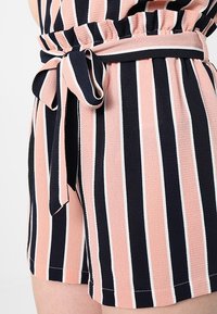 Randiga shorts i marinblått, rosa och vitt tyg. Har en rynkad midja med ett knytbälte och en mjuk, texturerad yta.