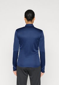 Μπλε ναυτικό τοπ με μακριά μανίκια, κατασκευασμένο από λείο, απαλό ύφασμα, με γιακά. Η πίσω όψη είναι εφαρμοστή, αναδεικνύοντας έναν κομψό, κομψό σχεδιασμό.