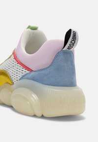 Baskets multicolores avec un mesh blanc, des accents en daim jaune, rose et bleu, et une semelle en caoutchouc translucide avec un détail de bande texturée.
