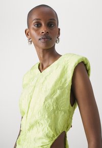 Robe sans manches vert citron avec une texture florale, décolleté en V et découpes sur les côtés. Présente des détails froncés sur les côtés pour un look ajusté.