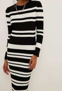 Abito a righe bianche e nere con maniche lunghe e silhouette aderente. Le righe alternano larghezze diverse per un design audace.