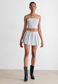 Grå cropped topp med spaghetti-stropper og en plissert miniskjørt. Begge plaggene har en glatt tekstur. Sorte ankelboots fullfører antrekket.