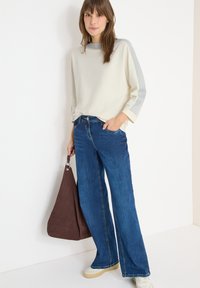 Vaalean beige, pitkähihainen paita, jossa on harmaita yksityiskohtia; siniset, leveälahkeiset farkut; ruskea laukku; valkoiset tennarit. Yksinkertainen muotoilu, rento tyyli.