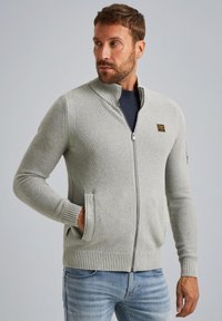 Lichtgrijze ritscardigan van textuurgebreid materiaal, met rib gebreide manchetten en onderste rand, zijzakken en een kleine logo-accent op de borst.