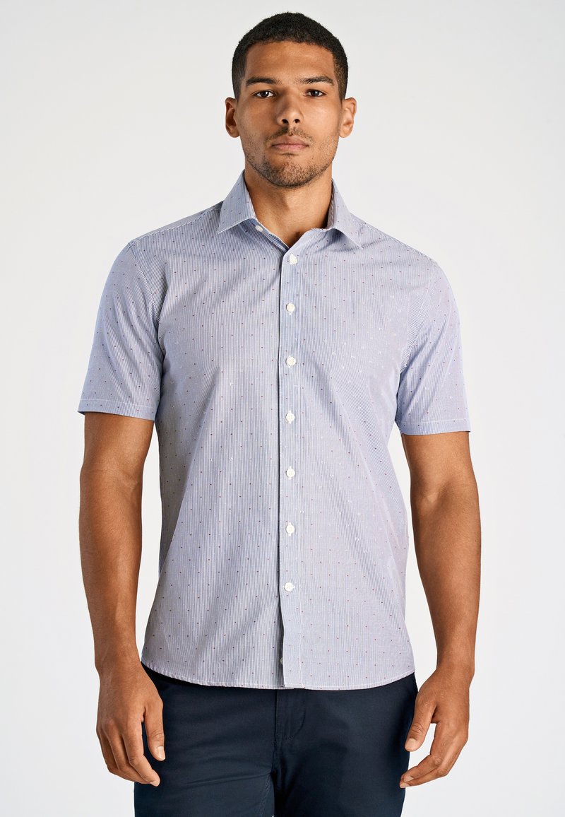 Camicia a maniche corte con bottoni di colore azzurro chiaro, con sottili righe e piccoli punti rossi. Presenta un colletto a punta e un orlo dritto.