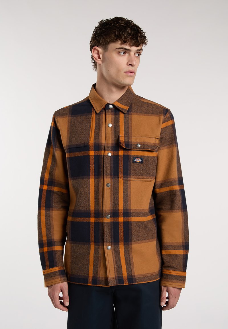 Camicia a quadri marrone e blu navy con colletto a punta, chiusura a bottoni, tasca sul petto e bottoni metallici, realizzata in un tessuto testurizzato.
