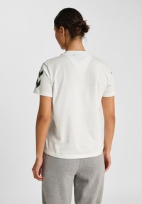 Hvid bomulds T-shirt med korte ærmer, der har sorte chevron mønstre på skuldrene og en klassisk rund halsudskæring.