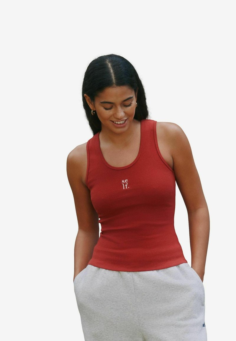 Canotta rossa a coste con scollo tondo e testo stampato "se lf." Abbinata a pantaloni della tuta grigi, con vestibilità slim e tessuto morbido.