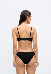 Σετ μαύρου μπικίνι με απλό σχέδιο, ρυθμιζόμενους ιμάντες και κλείσιμο με αγκράφα στο πίσω μέρος. Ομαλή υφή και μίνιμαλ σχεδιασμός.